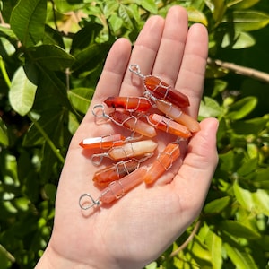 May include: A collection of carnelian crystal pendants wrapped in silver wire. The carnelian crystals are a mix of orange and red hues.