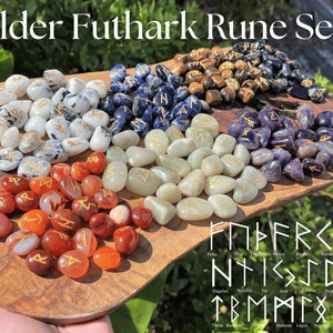 May include: A set of Elder Futhark runes on a wooden board. The runes are made of various stones, including clear, blue, green, purple, and red. Each rune is inscribed with a gold symbol. The runes are arranged in rows on the board, with the names of the runes listed below.