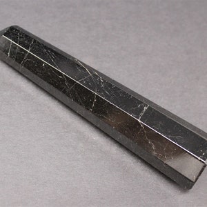 May include: A black obsidian point with a faceted, hexagonal shape. The point is polished and has a smooth, shiny surface.