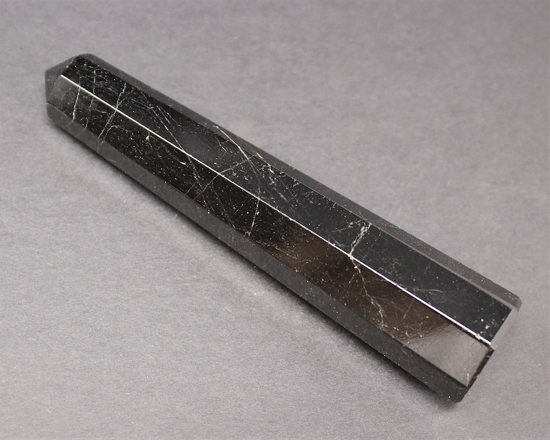 May include: A black obsidian point with a faceted, hexagonal shape. The point is polished and has a smooth, shiny surface.