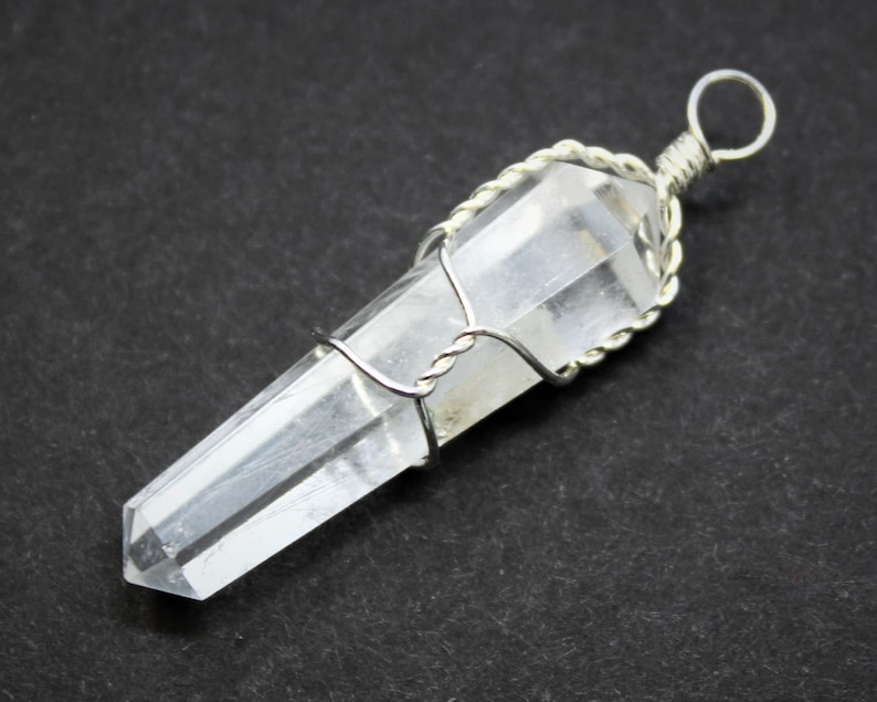 May include: A clear quartz crystal point pendant wrapped in silver wire. The pendant has a simple loop for attaching to a chain or cord.