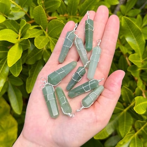 May include: A collection of green aventurine crystal points wrapped in silver wire. The points are all different sizes and shapes, and they are arranged in a hand.