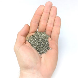 May include: A hand holding a pile of small, silver-colored metal pieces.