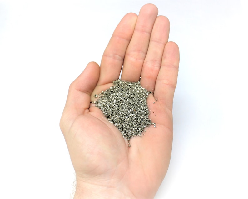 May include: A hand holding a pile of small, silver-colored metal pieces.