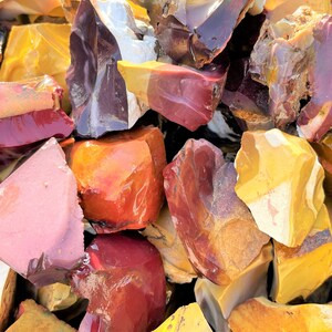 May include: A collection of raw, uncut gemstones in various colors. The stones display a range of hues, including deep reds, oranges, yellows, and pinks. The surfaces of the stones are rough and textured, with a natural, unpolished appearance.
