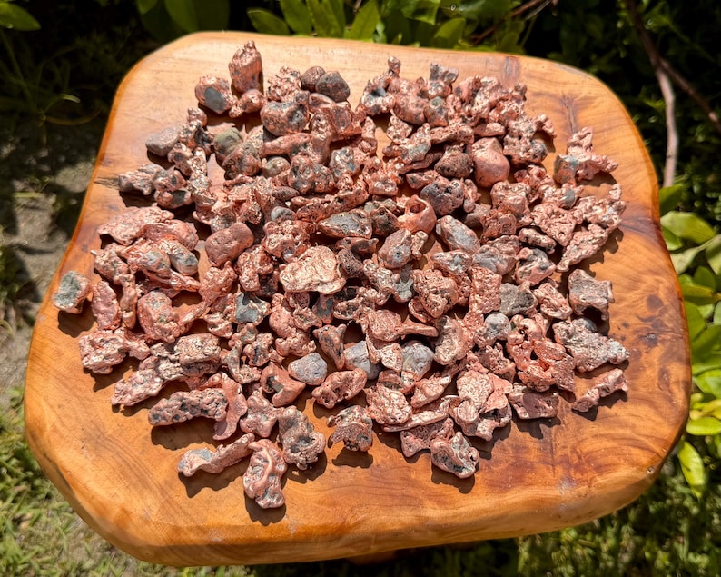 May include: A collection of numerous small, irregular copper nuggets with a metallic, reddish-brown finish. Each piece displays a unique, rough, and textured surface with varying shapes and sizes, showcasing the raw, unrefined appearance of the metal.