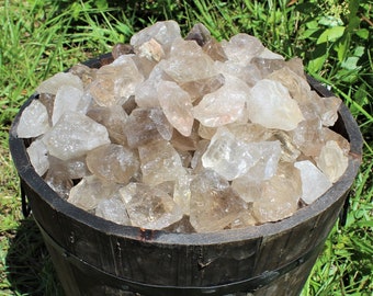 May include: A wooden bucket filled with a large quantity of raw, clear quartz crystals. The crystals are various sizes and shapes, with some having a smoky brown hue.