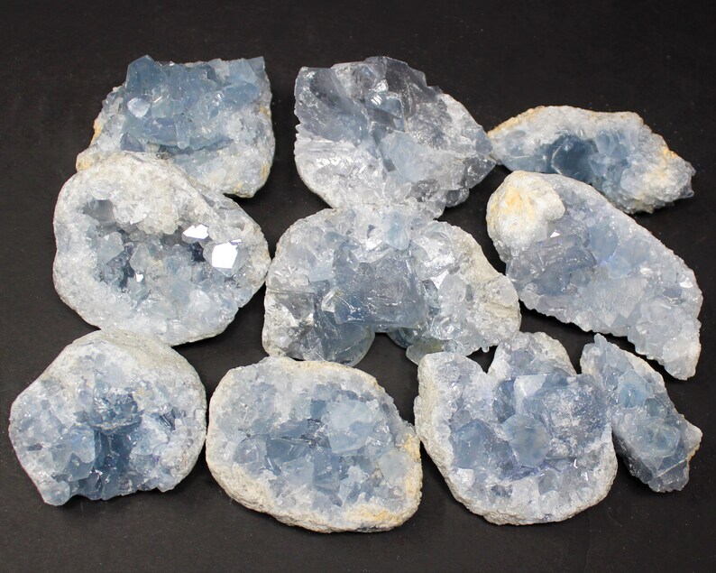 May include: A collection of ten blue celestite crystal clusters. The crystals are translucent and have a variety of shapes and sizes. The clusters are arranged in a random pattern on a black background.