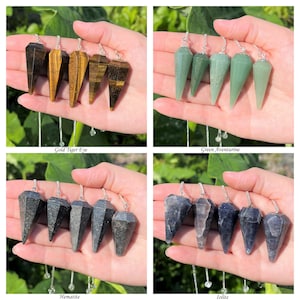 May include: Set of five crystal pendulums in four different colors: gold tiger eye, green aventurine, hematite, and iolite. Each pendulum is a pointed, faceted crystal on a silver chain.