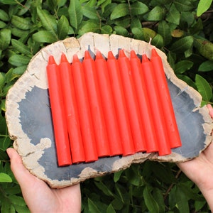 May include: A set of 12 bright orange candles arranged on a wooden slab. The candles are all the same size and shape, and they are arranged in a neat row.