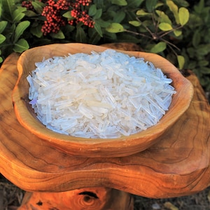 May include: A wooden bowl filled with clear quartz crystal points. The bowl is sitting on a wooden stand.