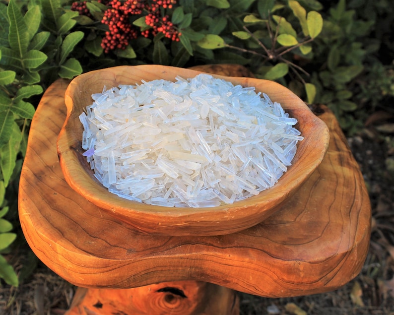 May include: A wooden bowl filled with clear quartz crystal points. The bowl is sitting on a wooden stand.
