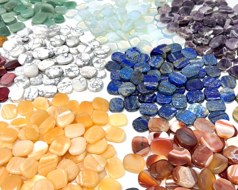 May include: A collection of polished gemstones in various colors, including green, white, blue, purple, orange, and red. The stones are oval-shaped and arranged in a circular pattern, showcasing their natural textures and hues. Ideal for jewelry making or crystal healing.