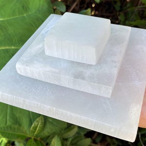 May include: Three white selenite charging plates stacked on top of each other. The plates are square and have a smooth, polished surface.