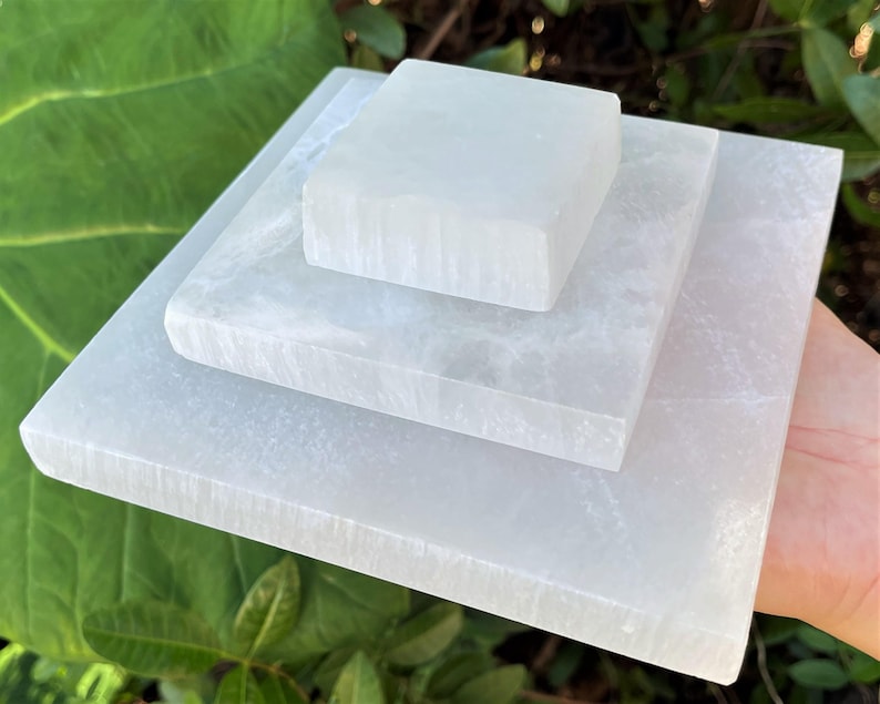 May include: Three white selenite charging plates stacked on top of each other. The plates are square and have a smooth, polished surface.