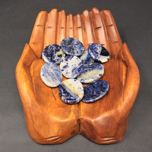 Op de afbeelding: Een houten handvormige schaal bevat een verzameling gepolijste stenen in blauw en wit. De stenen zijn glad en hebben een natuurlijke, organische uitstraling.