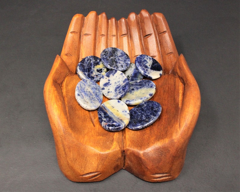 Op de afbeelding: Een houten handvormige schaal bevat een verzameling gepolijste stenen in blauw en wit. De stenen zijn glad en hebben een natuurlijke, organische uitstraling.