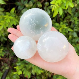 Op de afbeelding: Drie seleniet bollen in verschillende maten, met een gladde, witte en doorschijnende afwerking. De bollen zijn in een piramidevorm gerangschikt, met de grootste bol bovenaan.