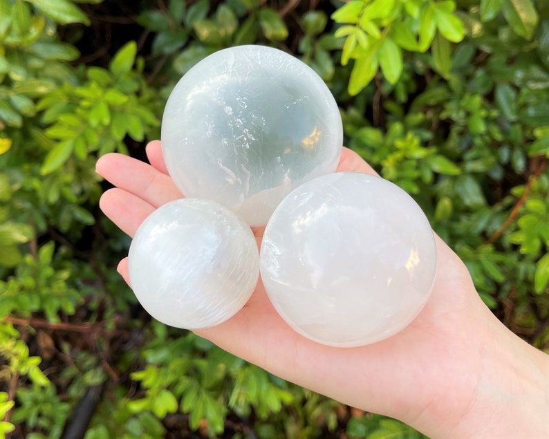 Op de afbeelding: Drie seleniet bollen in verschillende maten, met een gladde, witte en doorschijnende afwerking. De bollen zijn in een piramidevorm gerangschikt, met de grootste bol bovenaan.