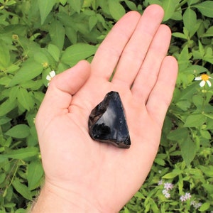 Puede incluir: Una gran roca de obsidiana negra con una forma irregular y rugosa. La roca est&aacute; siendo sostenida en la mano de una persona.