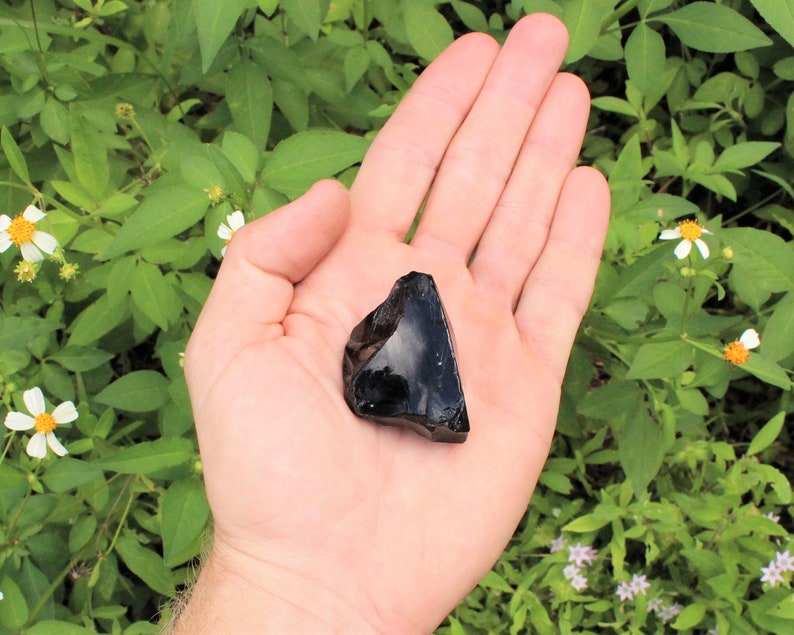 Puede incluir: Una gran roca de obsidiana negra con una forma irregular y rugosa. La roca est&aacute; siendo sostenida en la mano de una persona.