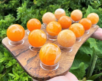 May include: A wooden serving tray holds a collection of orange spheres, each displayed on a clear stand. The spheres vary in shade from light yellow to deep orange, with a glossy, polished finish. The tray's wood grain adds a natural contrast to the vibrant spheres.