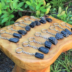 May include: A collection of black tourmaline crystal keychains. Each keychain features a raw, black tourmaline crystal attached to a silver chain and ring.