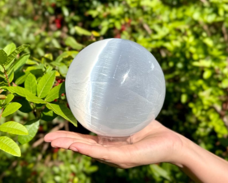 Op de afbeelding: Een grote, witte selenietbol met een glad, gepolijst oppervlak. De bol staat op een heldere standaard.