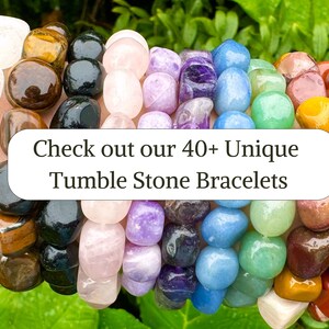 May include: A close-up of a variety of colorful tumbled stone bracelets. The bracelets are made with different types of stones, including clear quartz, tiger's eye, rose quartz, amethyst, blue lace agate, green aventurine, red jasper, and citrine. The text "Check out our 40+ Unique Tumble Stone Bracelets" is displayed on a white rectangle in the center of the image.