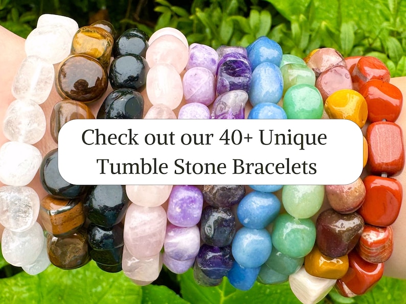 May include: A close-up of a variety of colorful tumbled stone bracelets. The bracelets are made with different types of stones, including clear quartz, tiger's eye, rose quartz, amethyst, blue lace agate, green aventurine, red jasper, and citrine. The text "Check out our 40+ Unique Tumble Stone Bracelets" is displayed on a white rectangle in the center of the image.