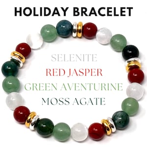 May include: A beaded bracelet with the text "HOLIDAY BRACELET". The bracelet features red, green, white, and dark green beads, with gold and silver accents. The text on the image reads: Selenite, Red Jasper, Green Aventurine, and Moss Agate.