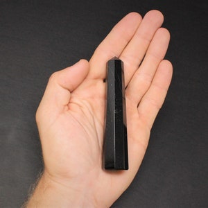 May include: Black obsidian crystal point, a dark, smooth, and pointed stone, held in a hand against a black background.