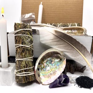 May include: A white candle with a lit flame, a sage bundle, a large feather, an abalone shell, and a small amethyst crystal are arranged with other items. The items are set against a white background, suggesting a spiritual or ritualistic theme.