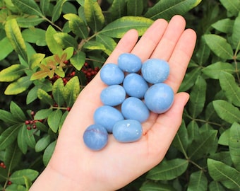 May include: A collection of smooth, light blue tumbled stones. The stones are various sizes and shapes, and they are arranged in a pile on a person's hand.