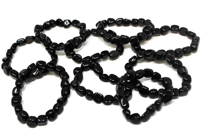 May include: A collection of five circular bracelets made from polished, smooth, black stone beads. Each bracelet is constructed from individual, irregularly shaped, glossy black pebbles strung together to form a continuous, flexible loop.