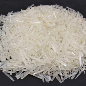 May include: A large pile of clear quartz crystals, also known as rock crystal, in a variety of sizes and shapes. The crystals are long and slender, with a translucent appearance.