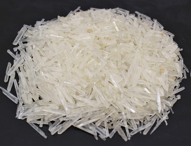 May include: A large pile of clear quartz crystals, also known as rock crystal, in a variety of sizes and shapes. The crystals are long and slender, with a translucent appearance.