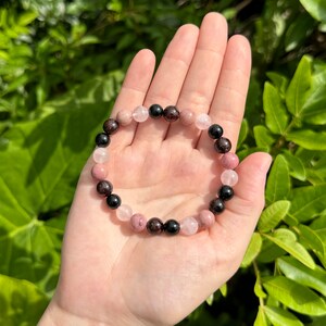 May include: A bracelet made of black, pink, and red gemstone beads. The bracelet is made of natural stones and is a beautiful piece of jewelry.