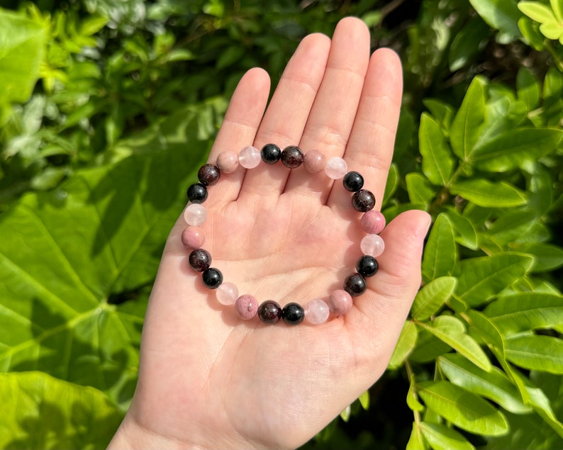 May include: A bracelet made of black, pink, and red gemstone beads. The bracelet is made of natural stones and is a beautiful piece of jewelry.