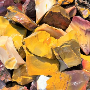 May include: A collection of raw, uncut stones in various shades of yellow, red, and cream. The stones have a rough, natural texture and appear to be freshly cut. The image is a close-up, showcasing the different colors and patterns within the stones.