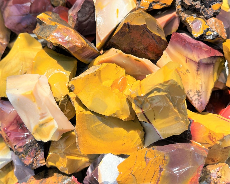 May include: A collection of raw, uncut stones in various shades of yellow, red, and cream. The stones have a rough, natural texture and appear to be freshly cut. The image is a close-up, showcasing the different colors and patterns within the stones.