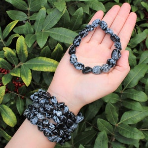 May include: Two bracelets made of black and white snowflake obsidian beads. The bracelets are stacked on a person's wrist.