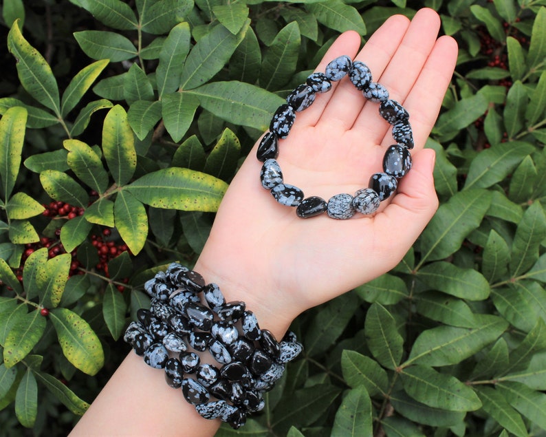 May include: Two bracelets made of black and white snowflake obsidian beads. The bracelets are stacked on a person's wrist.