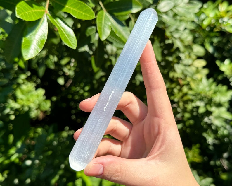 May include: A white selenite wand with a smooth, polished surface. The wand is about 6 inches long and has a rounded end.