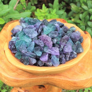 May include: A wooden bowl filled with a variety of green, blue, and purple fluorite crystals.