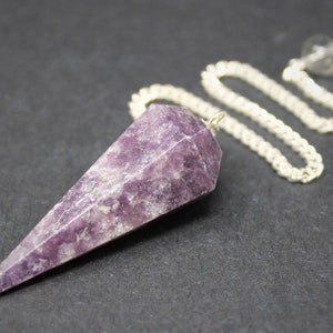 May include: A faceted, purple crystal pendulum with a silver chain and a small, clear bead at the top. The crystal is a deep shade of violet, with lighter streaks. The chain is a bright silver color. The pendulum is designed for divination.