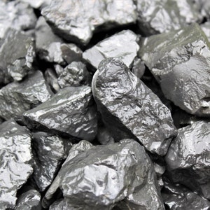 May include: A close-up of a pile of dark gray, smooth, and slightly wet rocks. The rocks are various sizes and shapes, and they are arranged in a random pattern.