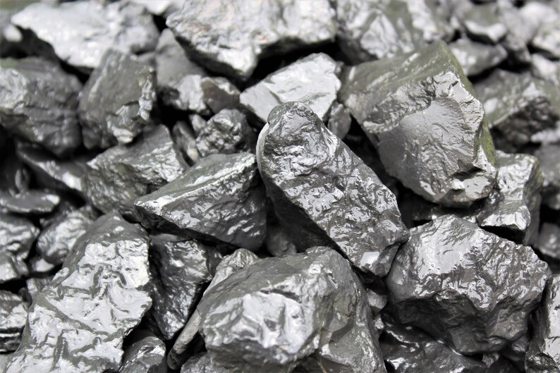 May include: A close-up of a pile of dark gray, smooth, and slightly wet rocks. The rocks are various sizes and shapes, and they are arranged in a random pattern.
