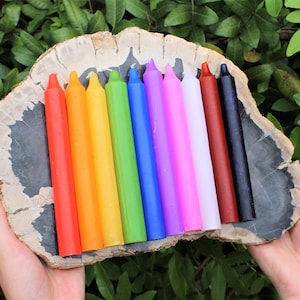 May include: A set of 10 colorful candles arranged in a rainbow pattern on a wooden slab. The candles are all the same size and shape, and they are made of a smooth, waxy material.
