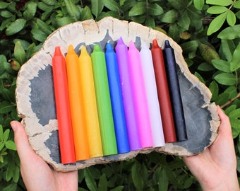 May include: A set of 10 colorful candles arranged in a rainbow pattern on a wooden slab. The candles are all the same size and shape, and they are made of a smooth, waxy material.